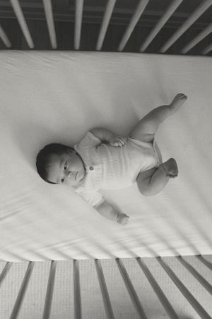 Black and white overhead view of a baby lying peacefully in a white crib.