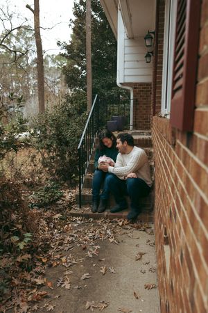 A couple sits together on porch steps surrounded by fallen autumn leaves.