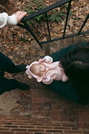 A sleeping baby in pink clothing rests on dark brick steps covered with fallen autumn leaves.