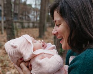 A joyful moment shared between parent and baby wearing pink knitwear among autumn trees.