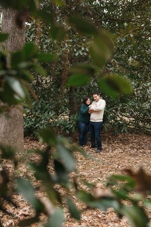Two people share a tender moment surrounded by trees and fallen leaves in a peaceful forest setting.