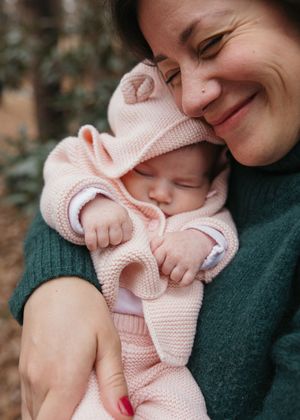 A tender moment between parent and sleeping baby wearing a pink knit outfit.