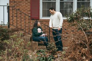 Two people having a conversation while sitting on brick steps outside a house in winter.
