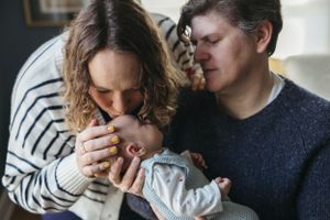 Two parents tenderly embrace their infant baby in an intimate family moment at home.