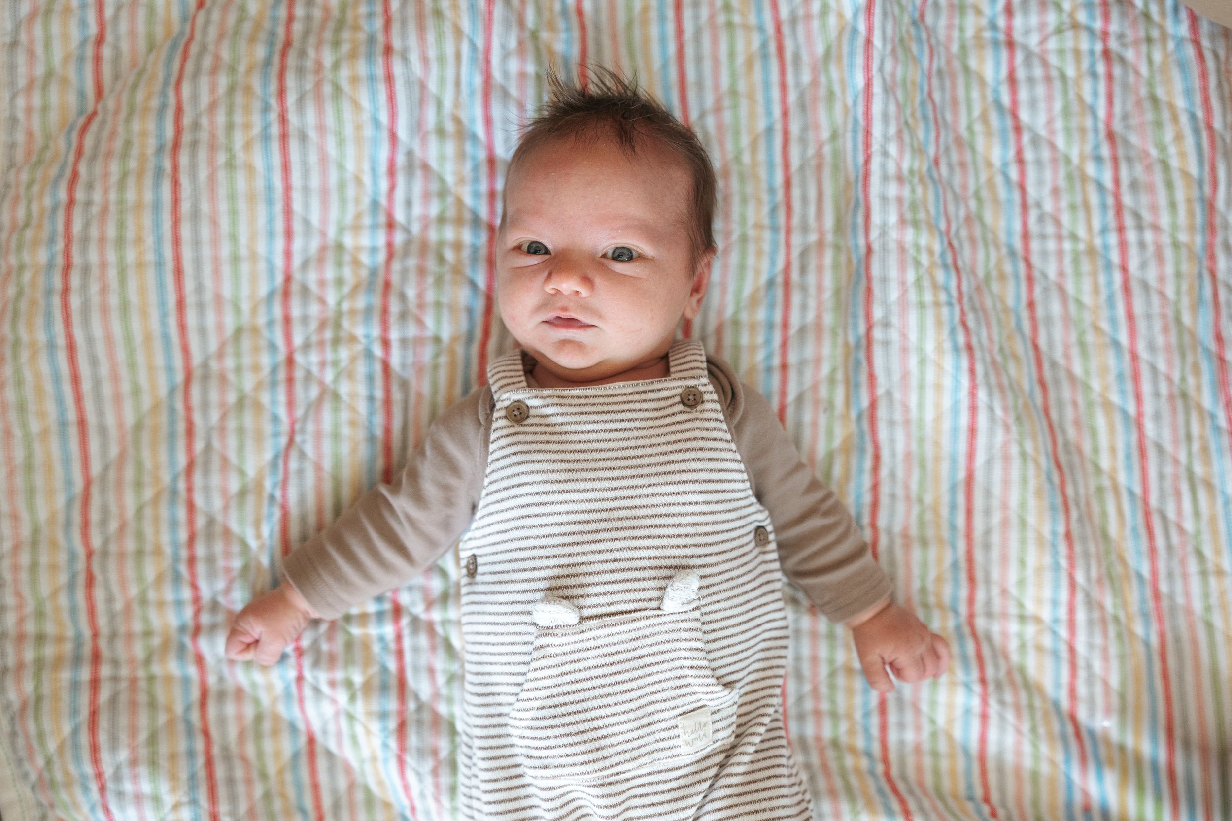 A baby lying on a striped blanket in a series of progressive shots showing different expressions.