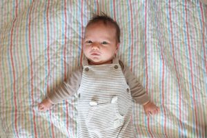 A baby lying on a striped blanket in a series of progressive shots showing different expressions.
