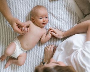 A newborn baby in a diaper lies on a striped blanket while a parent gently interacts with them.