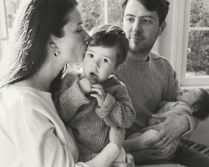 A black and white candid family moment showing parents with their young child in a cozy interior setting.
