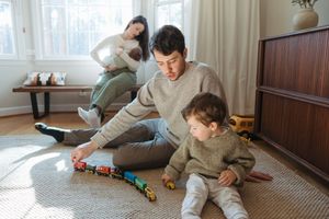 A cozy family moment playing with toy trains on a round rug in a sunlit living room.
