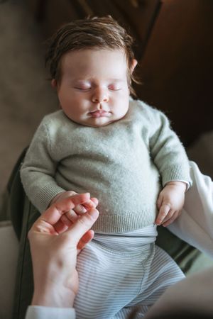 A sleeping baby in a mint green sweater and striped onesie rests peacefully in a series of connected photos.