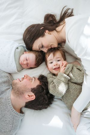 A sweet moment of family affection as they cuddle together on white bedding in natural light.