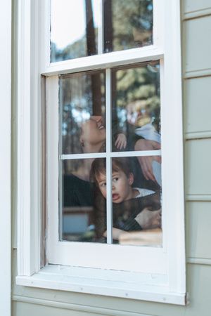 Children peer curiously through a white-framed window pane, creating a nostalgic scene of childhood wonder.