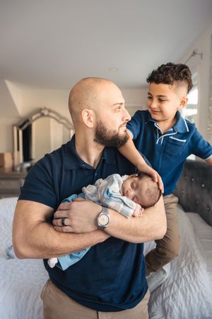A parent in a navy blue polo shirt holds and plays with a young child on a white bed.