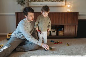 Parent and child spending quality time together playing with toys on a carpeted floor in a cozy home setting.