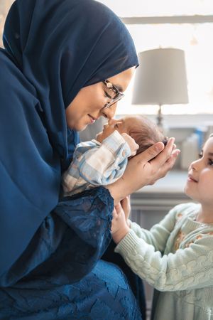 A healthcare provider in blue hijab and surgical mask examines a patient during a medical consultation.