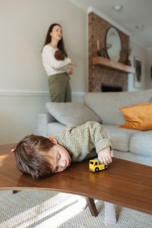 A sequence showing someone playfully peeking over and resting their head on a wooden table in a sunlit room.