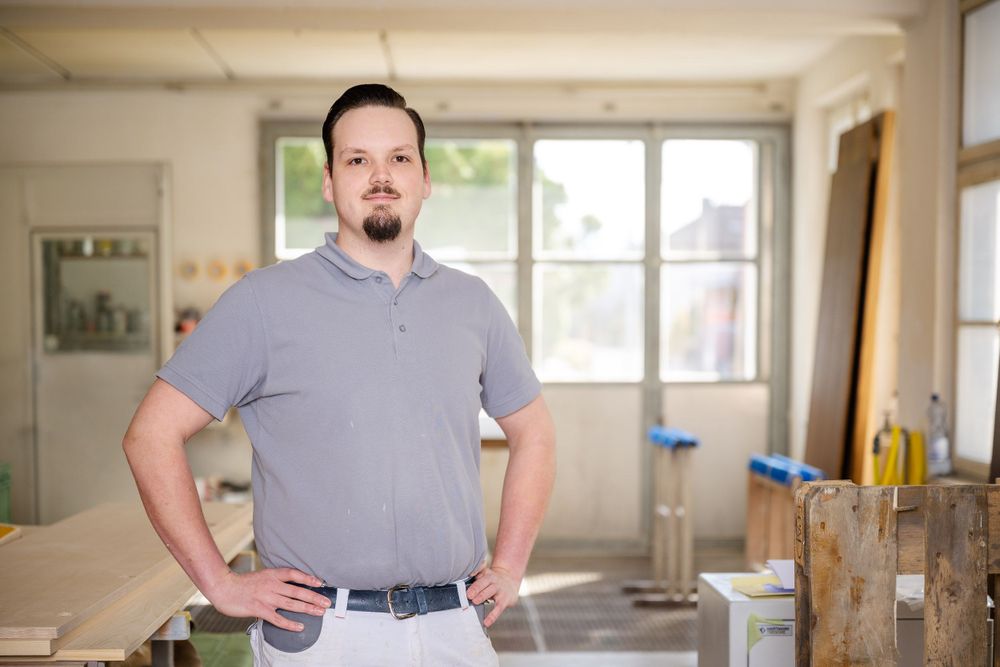 Workshop interior showing person in gray polo shirt standing near windows.