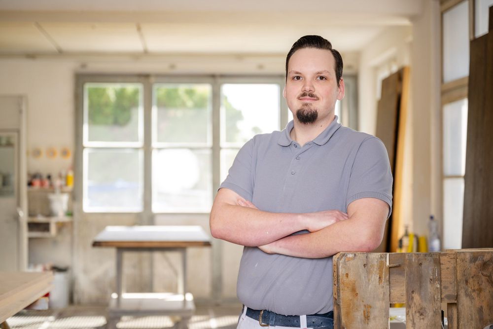 Person in casual attire posing confidently in bright workshop space.