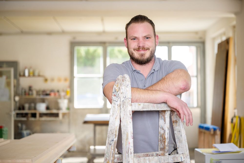 Workshop scene with person leaning on ladder in bright interior space.