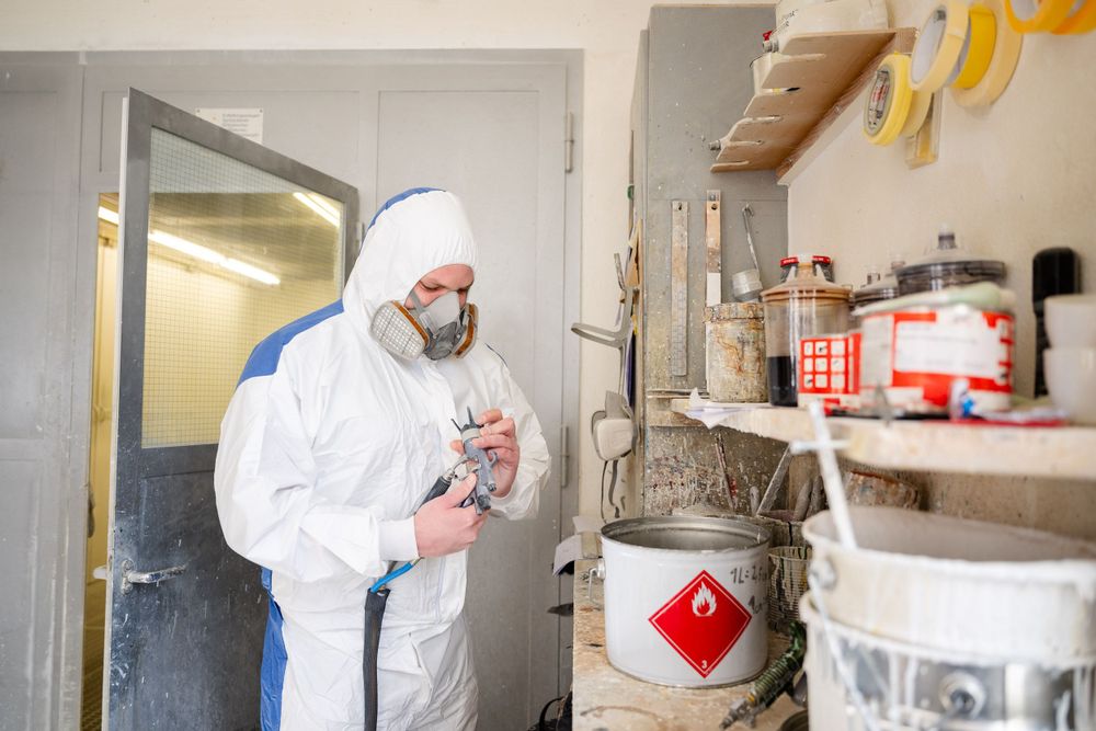 Worker in protective gear handling materials near storage shelves with hazard warning labels.