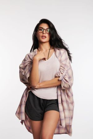 Jacqueline in an oversized beige jacket, wearing a crop top and black shorts, looking poised with soft lighting against a white backdrop.