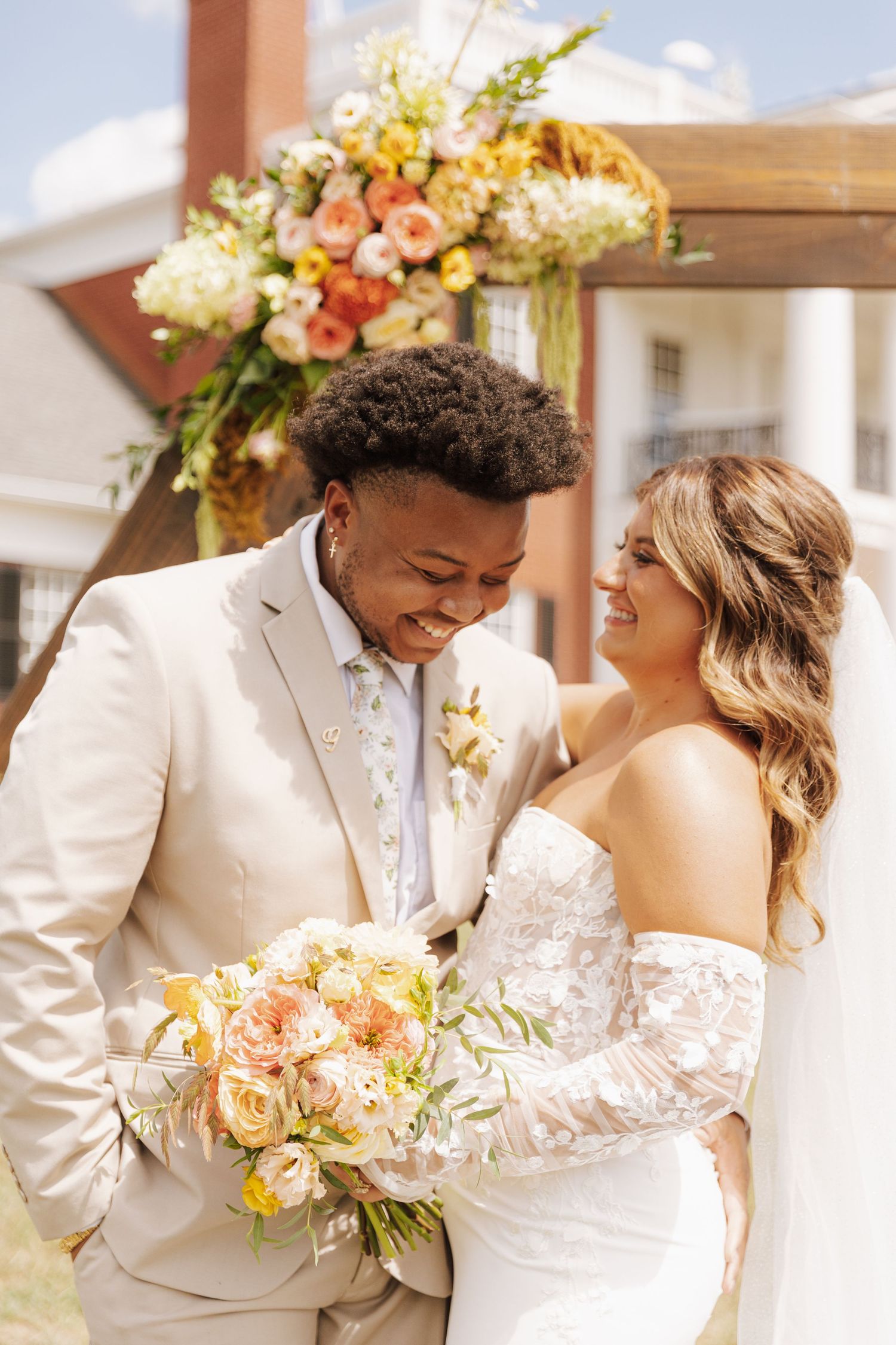 A happy couple shares a joyful moment outdoors on their wedding day with pastel floral arrangements.