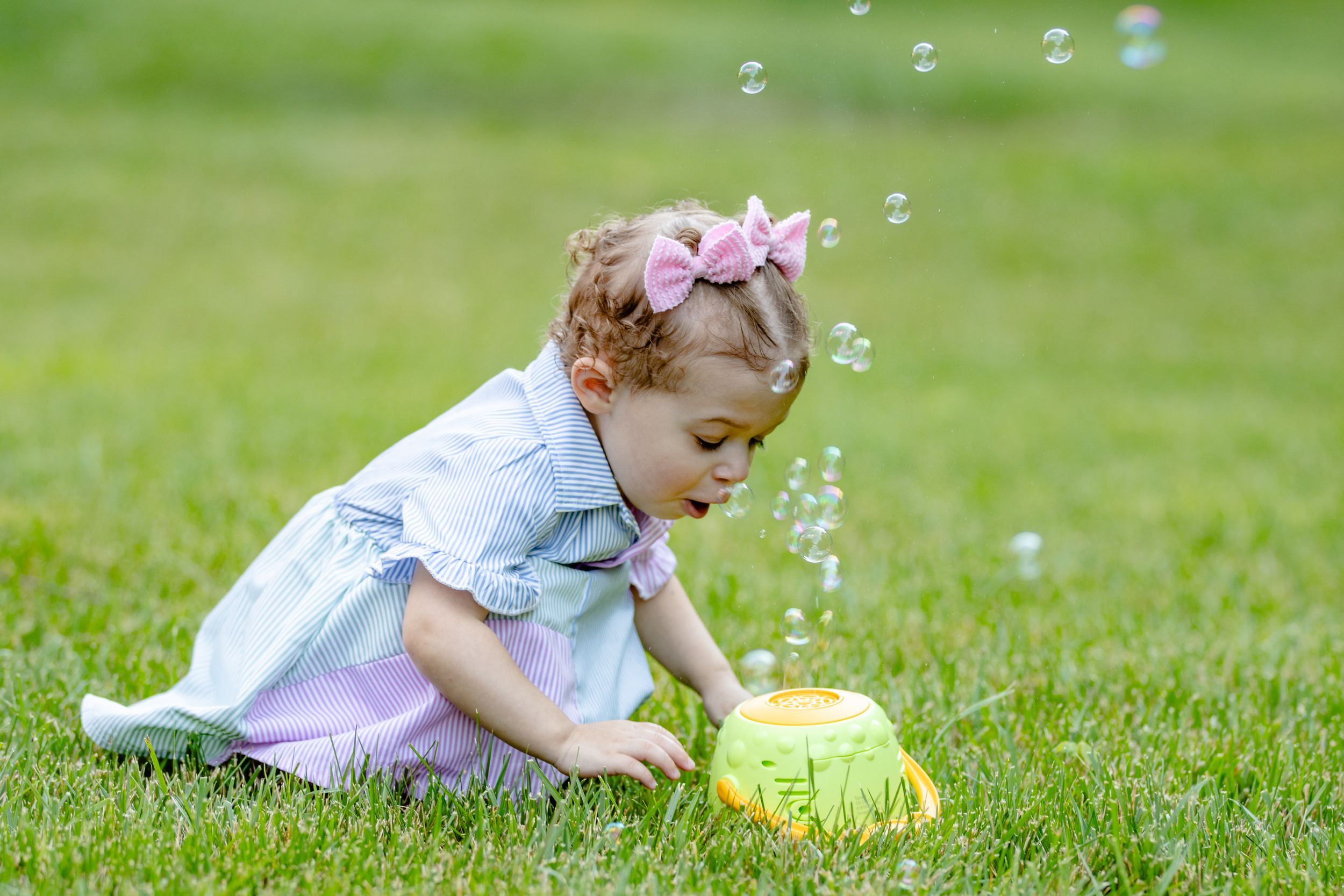 Child playing with soap bubbles on green grass lawn during springtime.