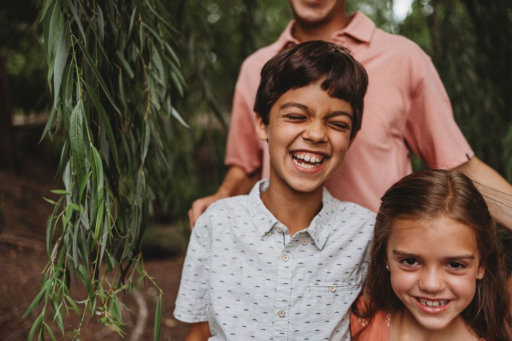 Two children laughing together under trees in casual attire.