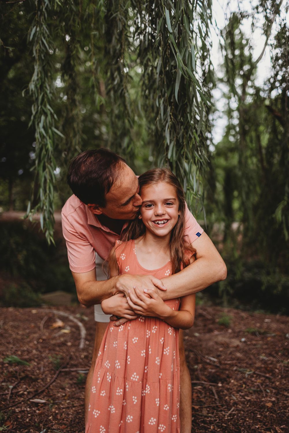 An intimate moment between parent and child under willow branches.