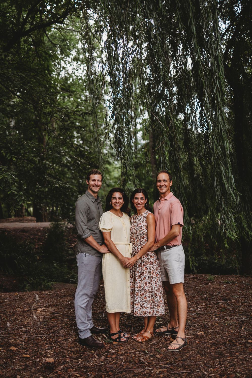 Two couples pose together for a group photo under drooping willow branches.