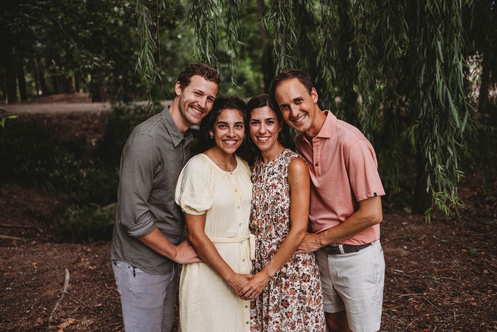 Group photo of four people embracing under willow trees on a forest path.
