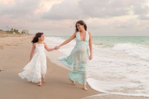 Pregnant mother and daughter walking hand in hand along the beach.