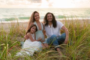 Happy family maternity portrait sitting in beach dunes with pregnant mother in mint dress at sunset.