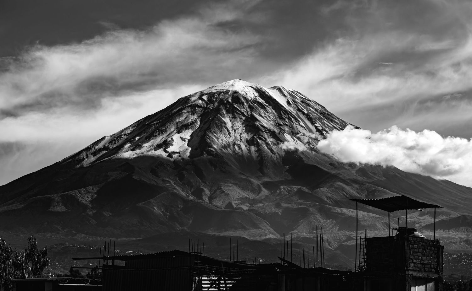 A dramatic black and white view of Misti Volcano rising above the landscape with cloudy skies.