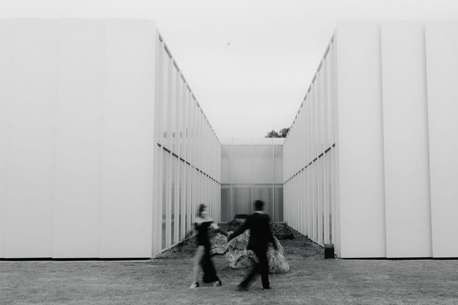 Minimalist white corridor with distant figures creating a sense of scale and perspective.