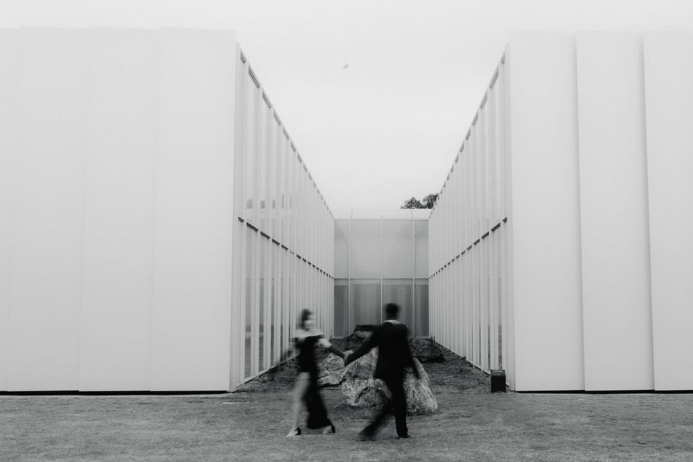 Minimalist white corridor with distant figures creating a sense of scale and perspective.