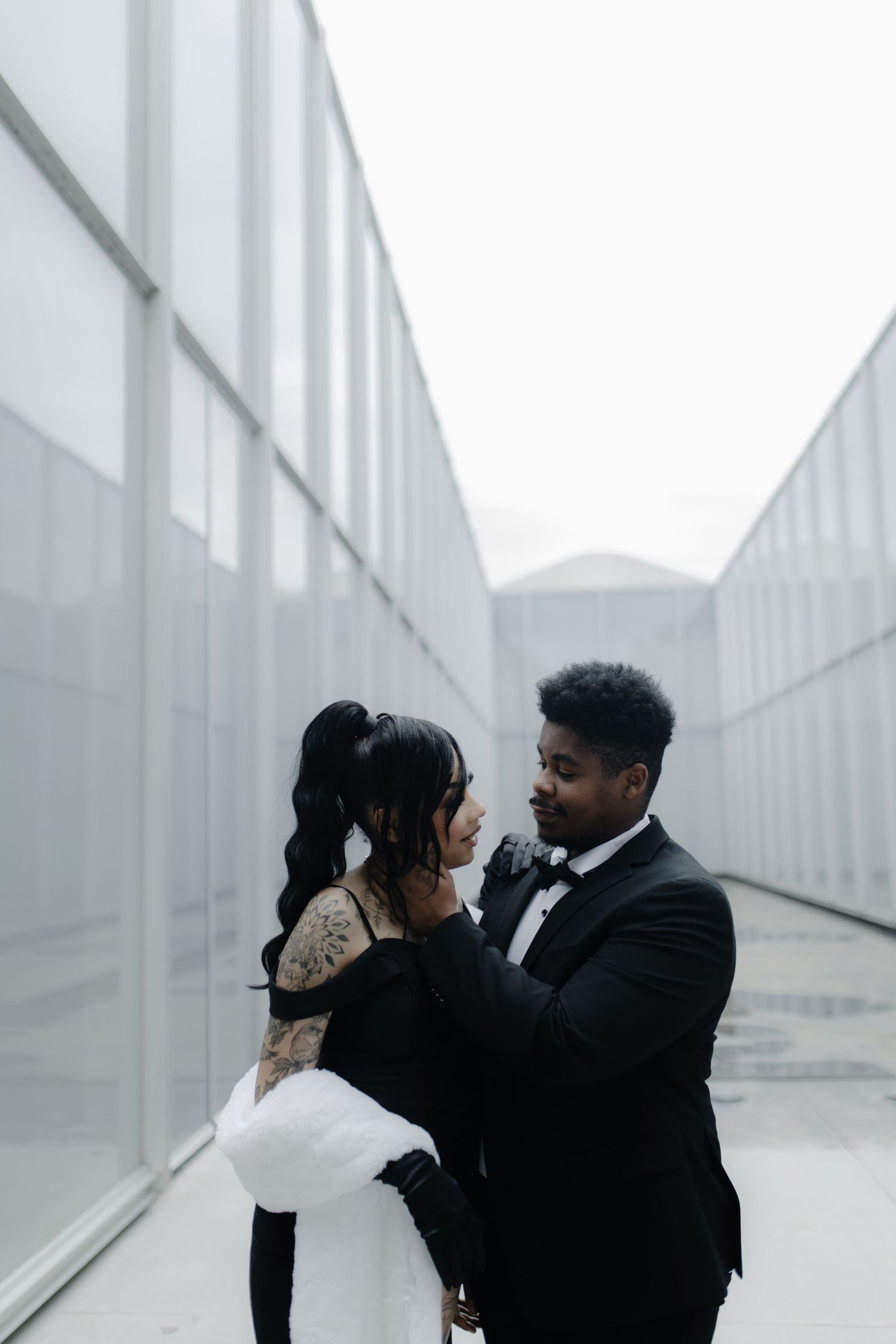A couple shares an intimate moment in front of white architectural walls.