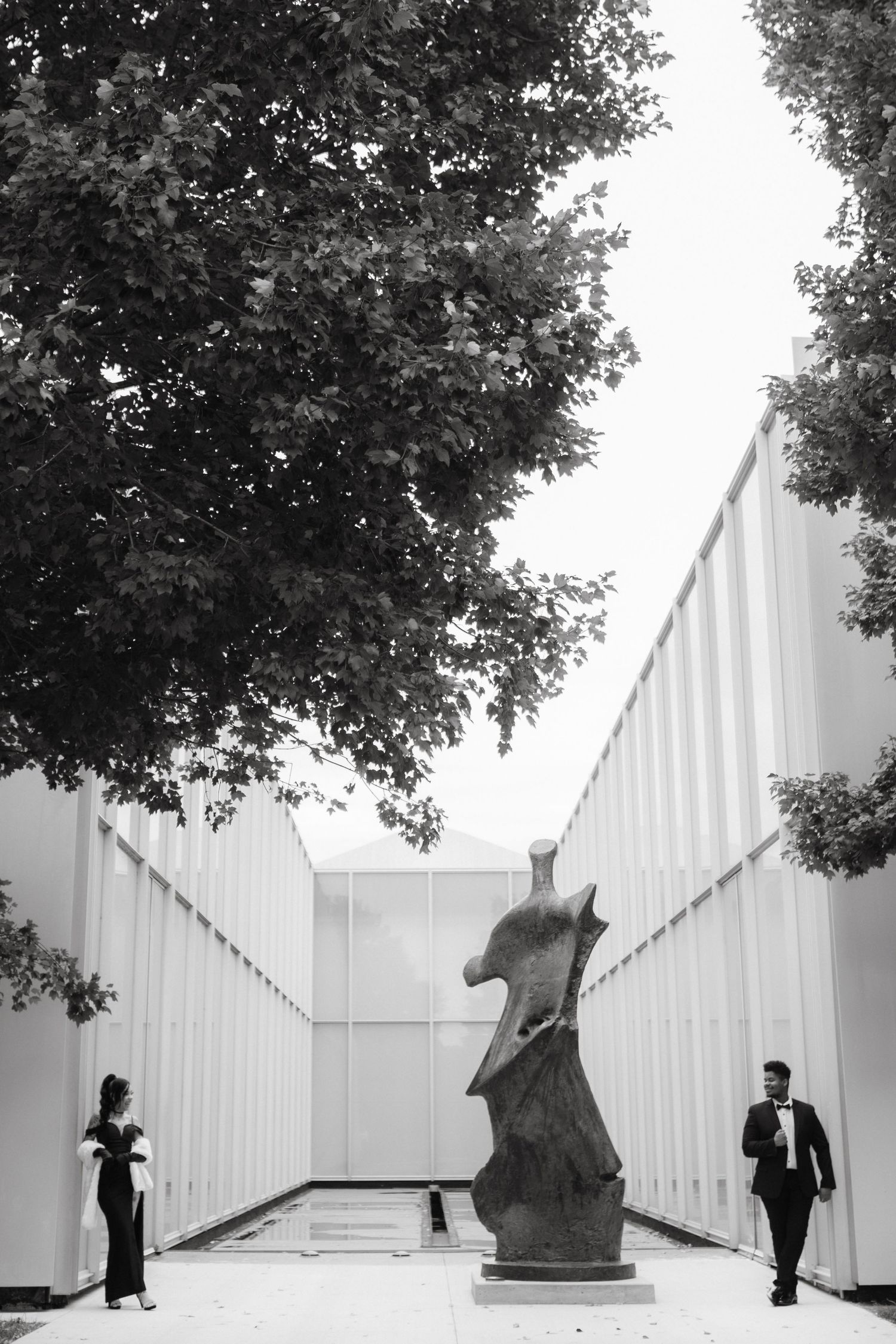 Two figures pose artistically between modern white walls and sculptures.