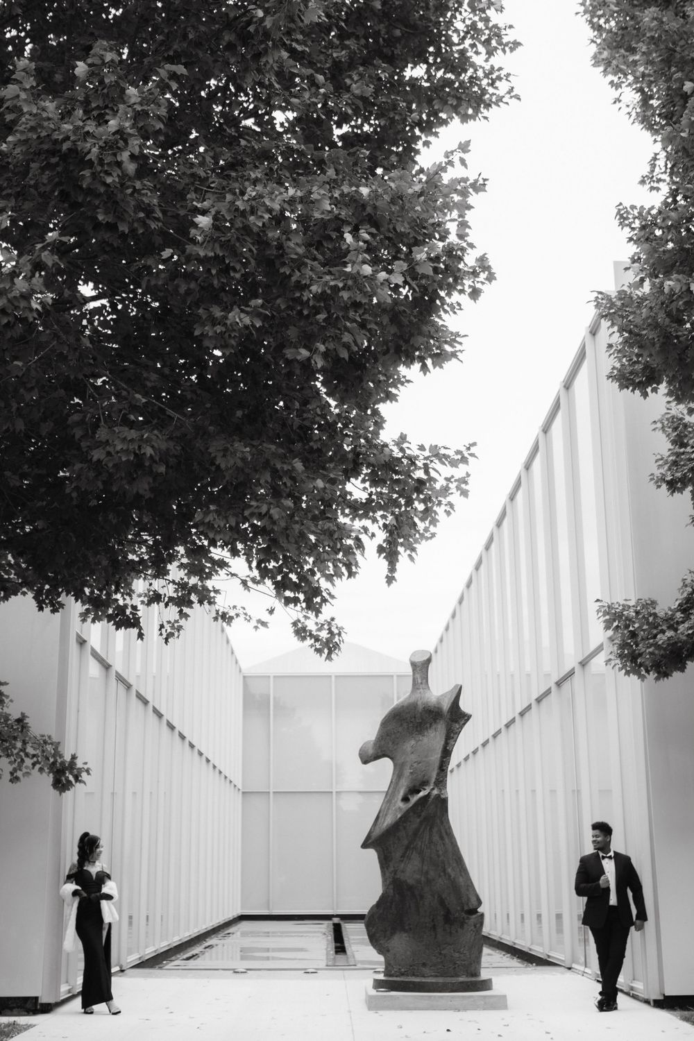 Two figures pose artistically between modern white walls and sculptures.