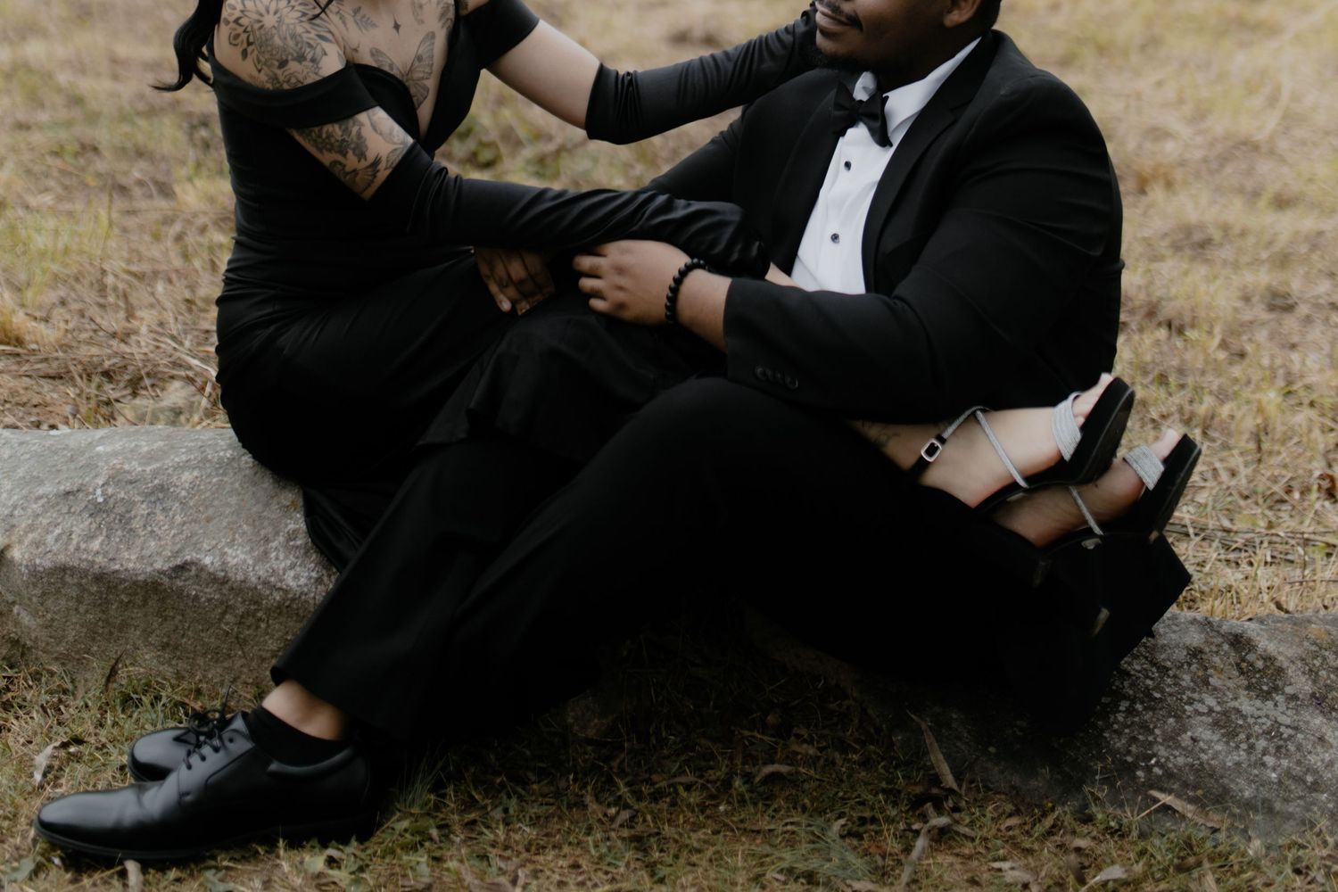 Close-up shot of formal black shoes and dress pants against a rustic outdoor backdrop.