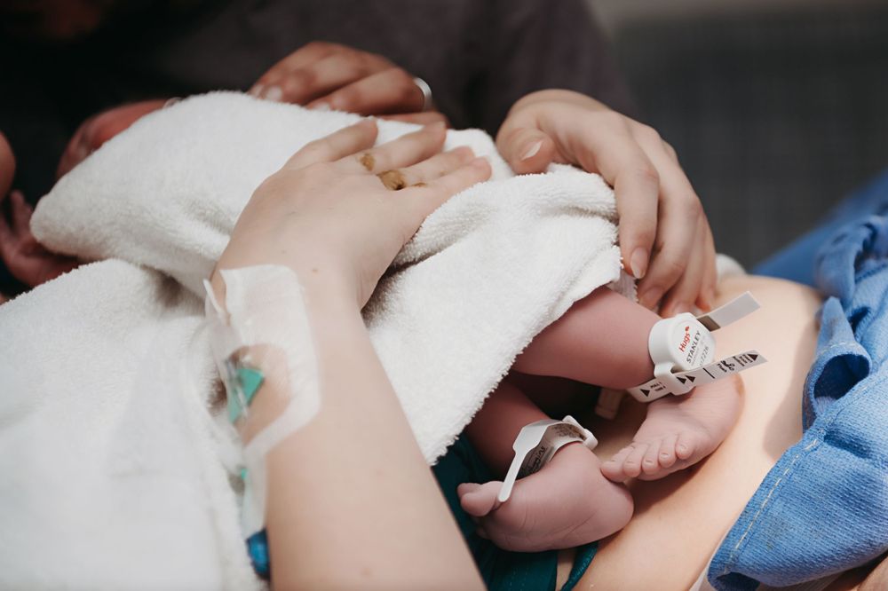 A newborn baby wrapped in white blankets receives medical care in a hospital setting.
