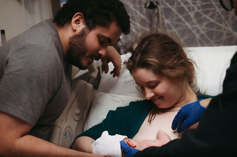 A tender moment as parents gaze lovingly at their newborn baby swaddled in blue blankets.