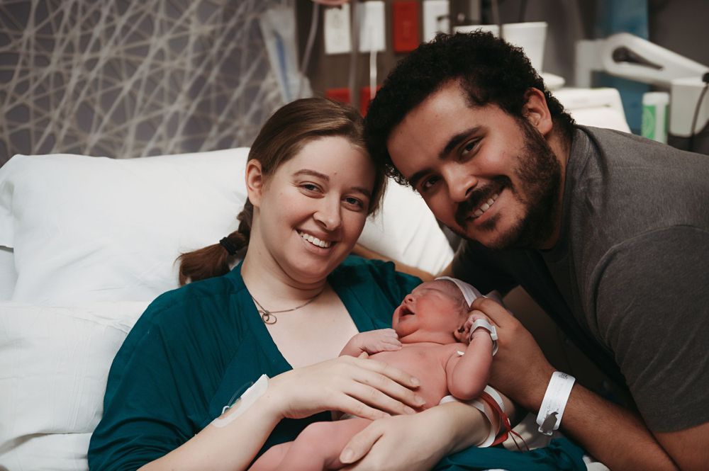 Happy couple holding their newborn baby while resting on hospital bed together.