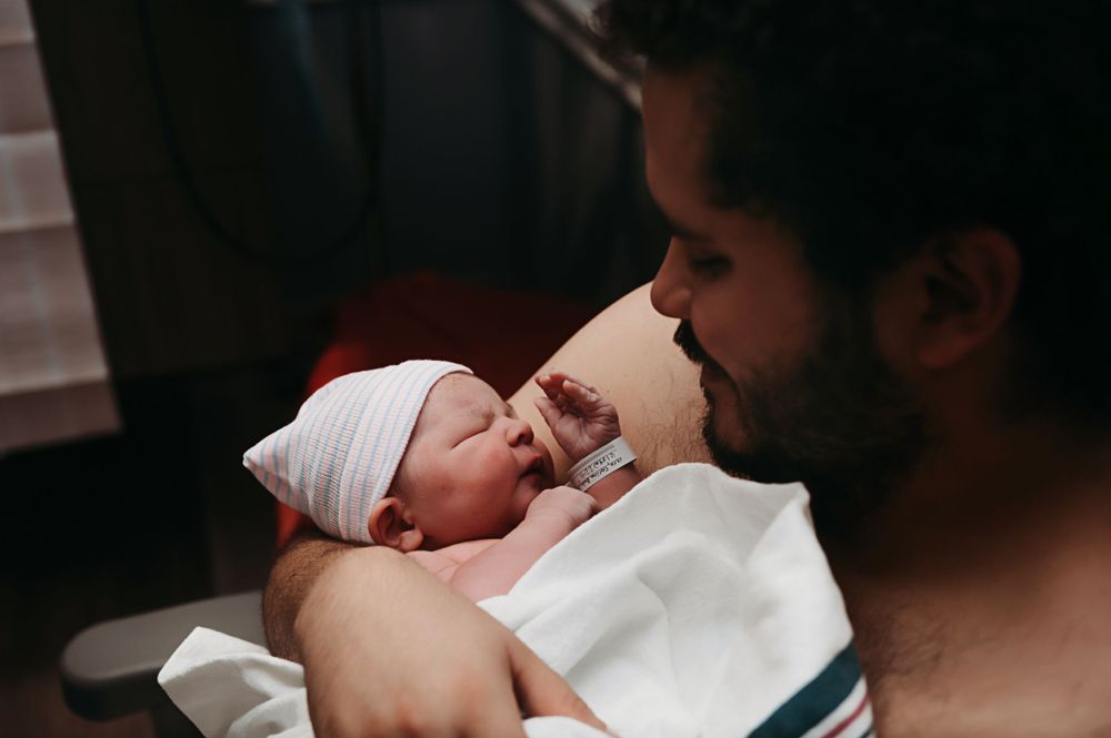 A tender moment between a parent and newborn baby wrapped in white blankets in a dimly lit room.