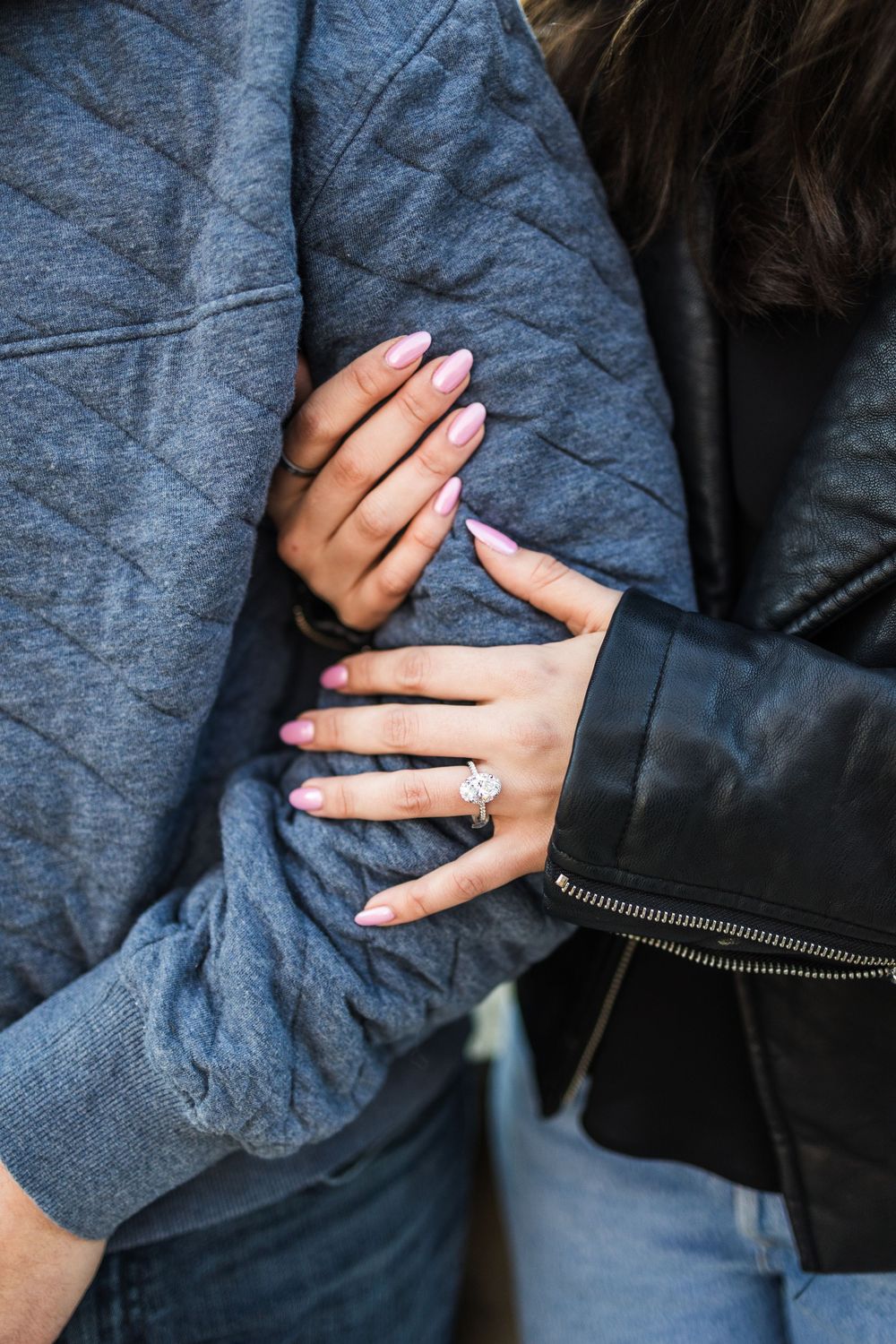 Close-up of engaged woman's hands showing diamond engagement ring while embracing partner.