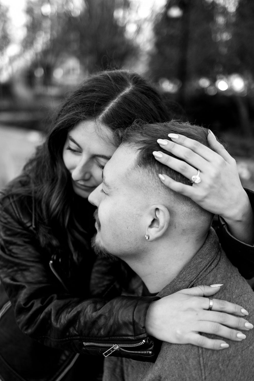 Black and white intimate photo of engaged couple embracing, woman showing diamond ring.