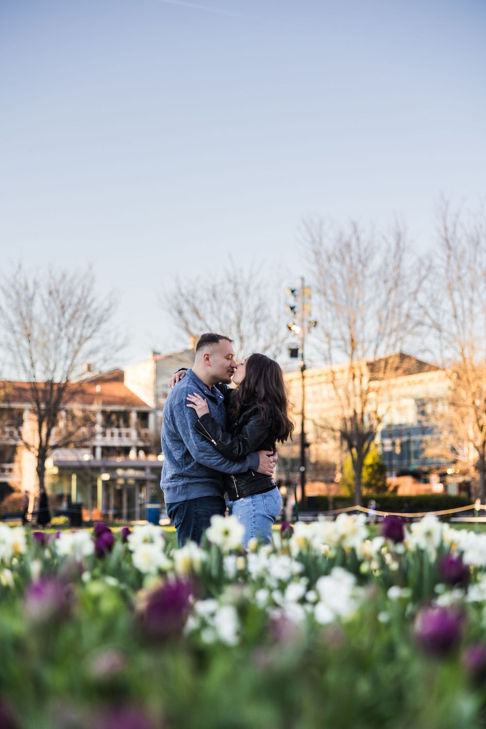 Couple sharing a romantic kiss surrounded by colorful tulips and daffodils at golden hour.