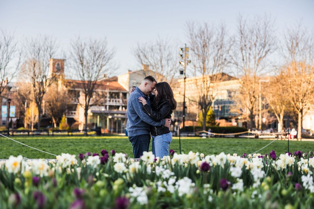 Couple embracing in a park surrounded by blooming white and purple flowers during golden hour.