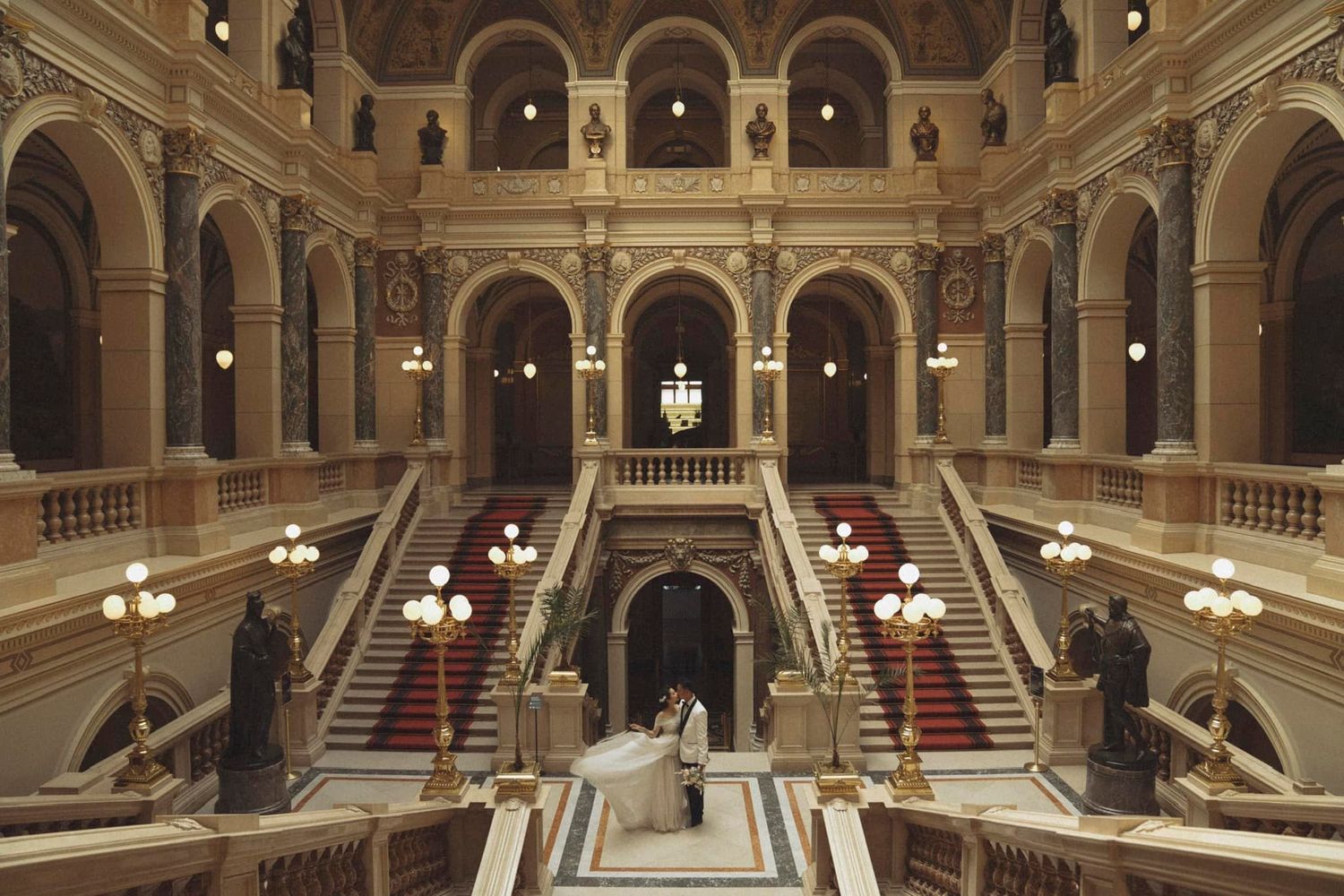 Grand ornate staircase in historic building with elegant architectural details and warm lighting.
