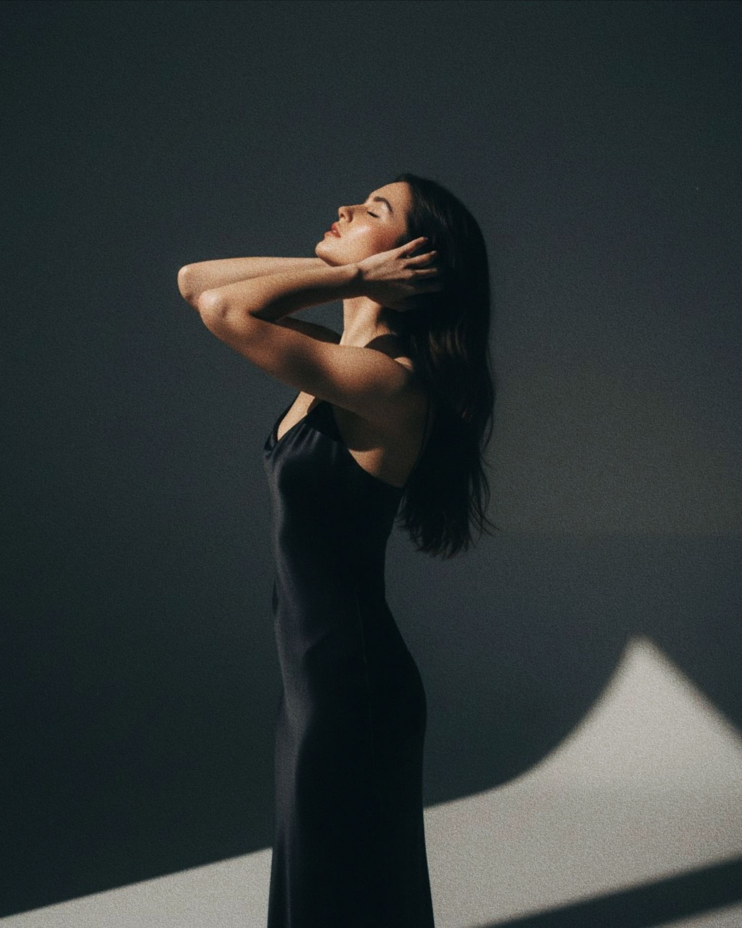 A figure in black clothing performs an expressive dance movement against a dramatic shadowed backdrop.